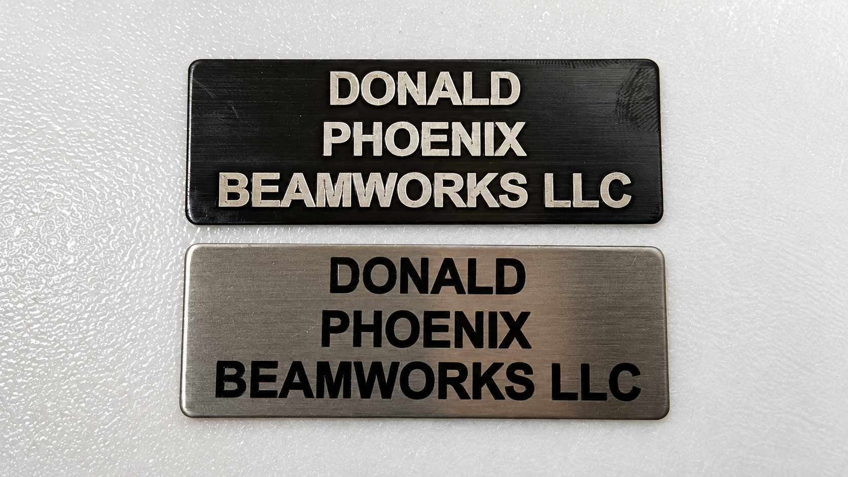 Phoenix Beamworks black and brushed metal name badge samples engraved with the company name